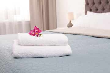Stack of fresh towels with flowers on bed in hotel room