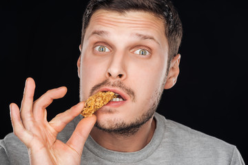 handsome man eating chicken nugget while looking at camera isolated on black