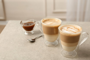 Glass cups of tasty caramel macchiato and gravy boat with syrup on table. Space for text