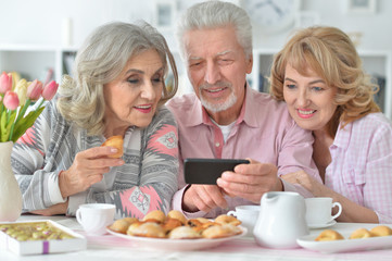 Portrait of happy senior people with smartphone drinking tea