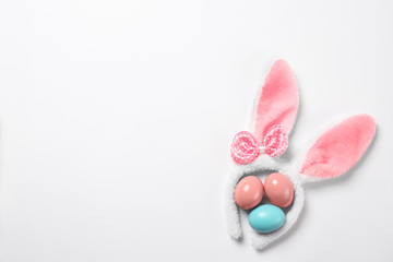 Funny headband with Easter bunny ears and dyed eggs white background, top view
