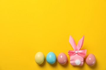 Flat lay composition of Easter bunny gift bag and dyed eggs on color background. Space for text