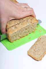 Baking bread at home. A loaf of freshly baked wholegrain bread with sunflower seeds lies on a cutting board. A woman cuts it with a knife.