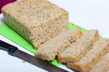 Baking bread at home. A loaf of freshly baked wholegrain bread with sunflower seeds lies on a cutting board. Bread slices and a knife are visible.
