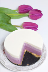 Blueberry cheesecake. A piece of ready-made dessert on a saucer. Jelly layers of different colors are visible. Near a cup of coffee and a bouquet of tulips.