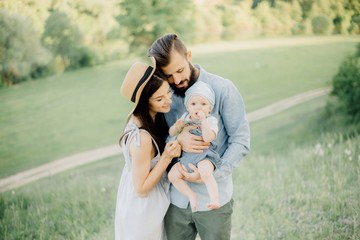 Happy family outdoor in spring. A stylish father with a beard keeps a daughter in his arms with his wife