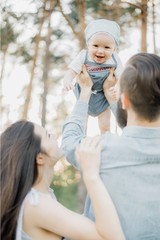 Happy family outdoor in spring. A stylish father with a beard keeps a daughter in his arms with his wife