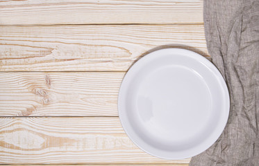 Obraz na płótnie Canvas Empty white plate and gray napkin on a wooden background, top view.