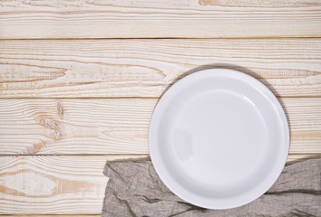 Fototapeta na wymiar Empty white plate and gray napkin on a wooden background, top view.