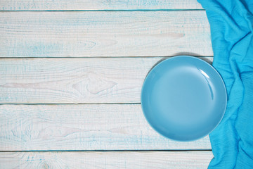 Empty blue plate and  blue napkin on a wooden background, top view.