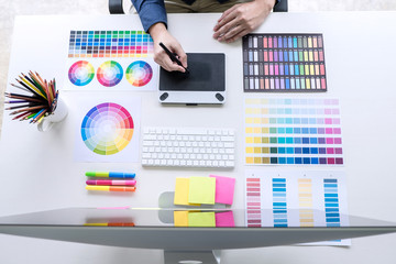 Image of male creative graphic designer working on color selection and drawing on graphics tablet at workplace with work tools and accessories, top view workspace