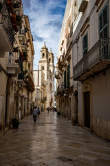 Fototapeta na wymiar ALTAMURA, ITALY - AUGUST 26, 2018: People passing by Santa Maria Assunta Cathedral in the historical center of Altamura in Puglia region. Moody cloudy summer afternoon, narrow vertical street view