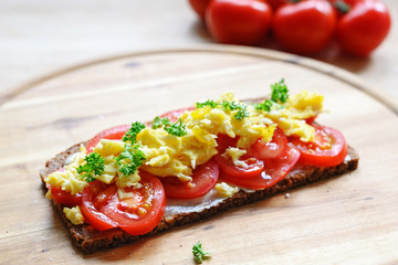 wholemeal bread with tomatoes, scrambled eggs and parsley garnish on a wooden board, copy space