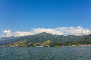Lake Phewa on the background of a green mountain valley and the snowy top of Mount Annapurna under a blue sky, view from the water
