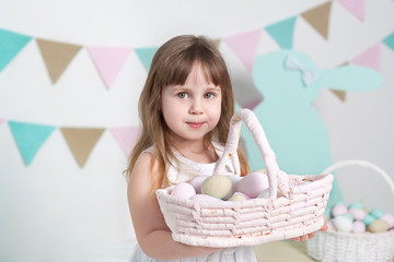 Easter 2019 Beautiful little girl in a white dress is standing with an Easter basket. Many different colorful Easter eggs, colorful interior. Close-up portrait of a child's face. Easter bunny 