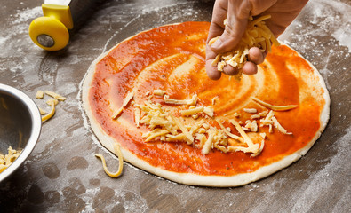 Man adding cheese to pizza at kitchen