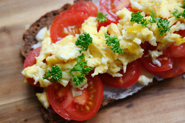 wholemeal bread with tomatoes, scrambled eggs and parsley garnish on a wooden board,top view from above, selected focus, narrow depth of field