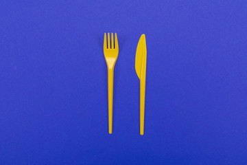 Tableware set of yellow plastic fork and knife isolated on blue background