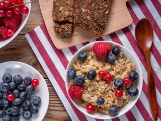 Top view of porridge with blueberries and raspberries and grain bread on wooden background. Vegan breakfast.