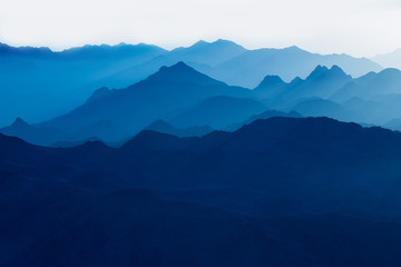 Beautiful view from the mountain. Panorama. Mountain range with visible silhouettes through the morning blue fog.