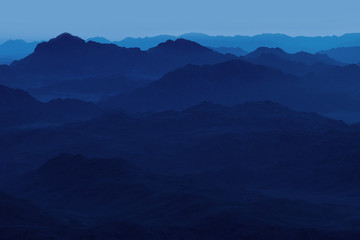 Beautiful view from the mountain. Panorama. Mountain range with visible silhouettes through the morning blue fog.