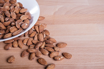 Pile of almonds in white dish on wooden floor.