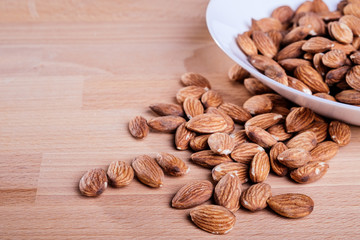 Pile of almonds in white dish on wooden floor.