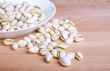 Pistachio nuts in white dish on wooden table