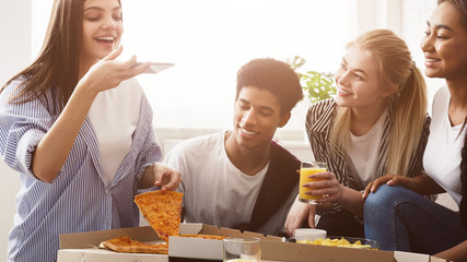 Young blogger taking photo of pizza, having party with friends