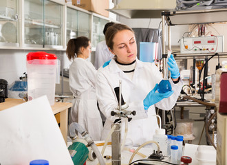 Female chemist analyzing liquid in test flasks