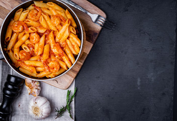 penne pasta with shrimps, tomato sauce   in a black frying pan with spice ,top view.