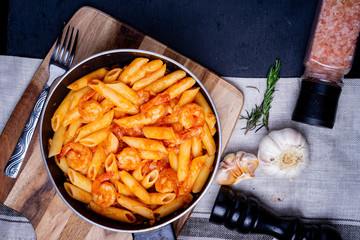 penne pasta with shrimps, tomato sauce   in a black frying pan with spice ,top view.