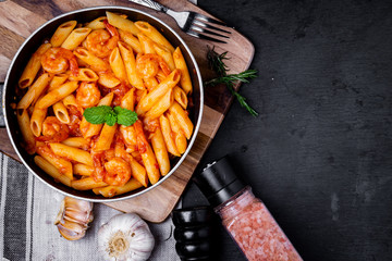 penne pasta with shrimps, tomato sauce   in a black frying pan with spice ,top view.