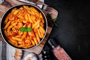 penne pasta with shrimps, tomato sauce   in a black frying pan with spice ,top view.
