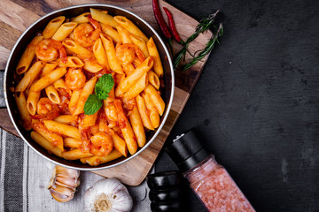 penne pasta with shrimps, tomato sauce   in a black frying pan with spice ,top view.