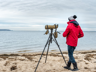 Young man on the beach watching birds life using telescope