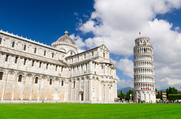 Pisa Cathedral Duomo Cattedrale and Leaning Tower Torre on Piazza del Miracoli square green grass lawn, blue sky with white clouds background in sunny day, Tuscany, Italy