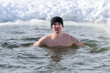 A man in a hat swims in the winter hole