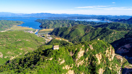 Obraz premium Aerial view of mountain with water reservoir on the background. Mountain peak with beautiful blue sky and green forest. Landscape of mountain in natural reserve park. Miyun, Beijing, China.