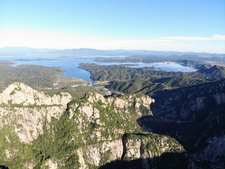 Aerial view of mountain with water reservoir  on the background. Mountain peak with beautiful blue sky and green forest. Landscape of mountain in natural reserve park. Miyun, Beijing, China.