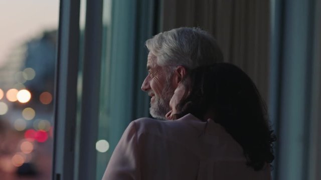 happy couple hugging at home looking out window at sunset enjoying successful retirement lifestyle on vacation sharing romantic connection
