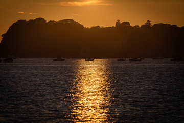 Naklejka premium Sunset reflecting on waves and boats in harbour