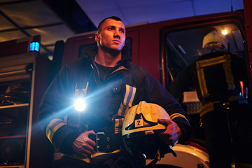 The fire brigade came to the call at night. Handsome fireman wearing a protective uniform with a...