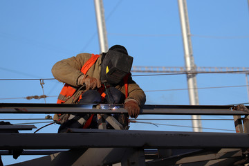 Welder working on scaffolding. Construction worker against the blue sky background, welding works
