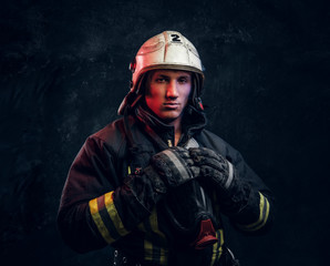 Firefighter in uniform and safety helmet posing in a dark studio, looking at the camera with a confident look.