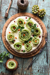 Raw vegetarian healthy dessert. Homemade pie with kiwi roses, berries, mint and cream filling on nutty crust served wth carved kiwis on blue background