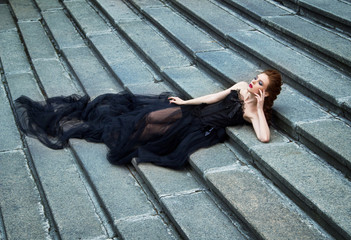 Art work Gothic fashion: a beautiful young girl in black dress and headwear sitting near castle....
