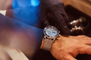 Close-up hands. Assistant helps the client to try on exclusive men's watches.