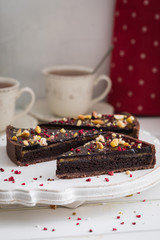 Sliced homemade chocolate tart on wooden plate background, with tea cups