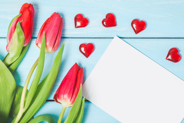 Colorful spring tulip flowers with blank photo and decorative red hearts on light blue wooden background as greeting card. Mothersday, love or spring concept.
